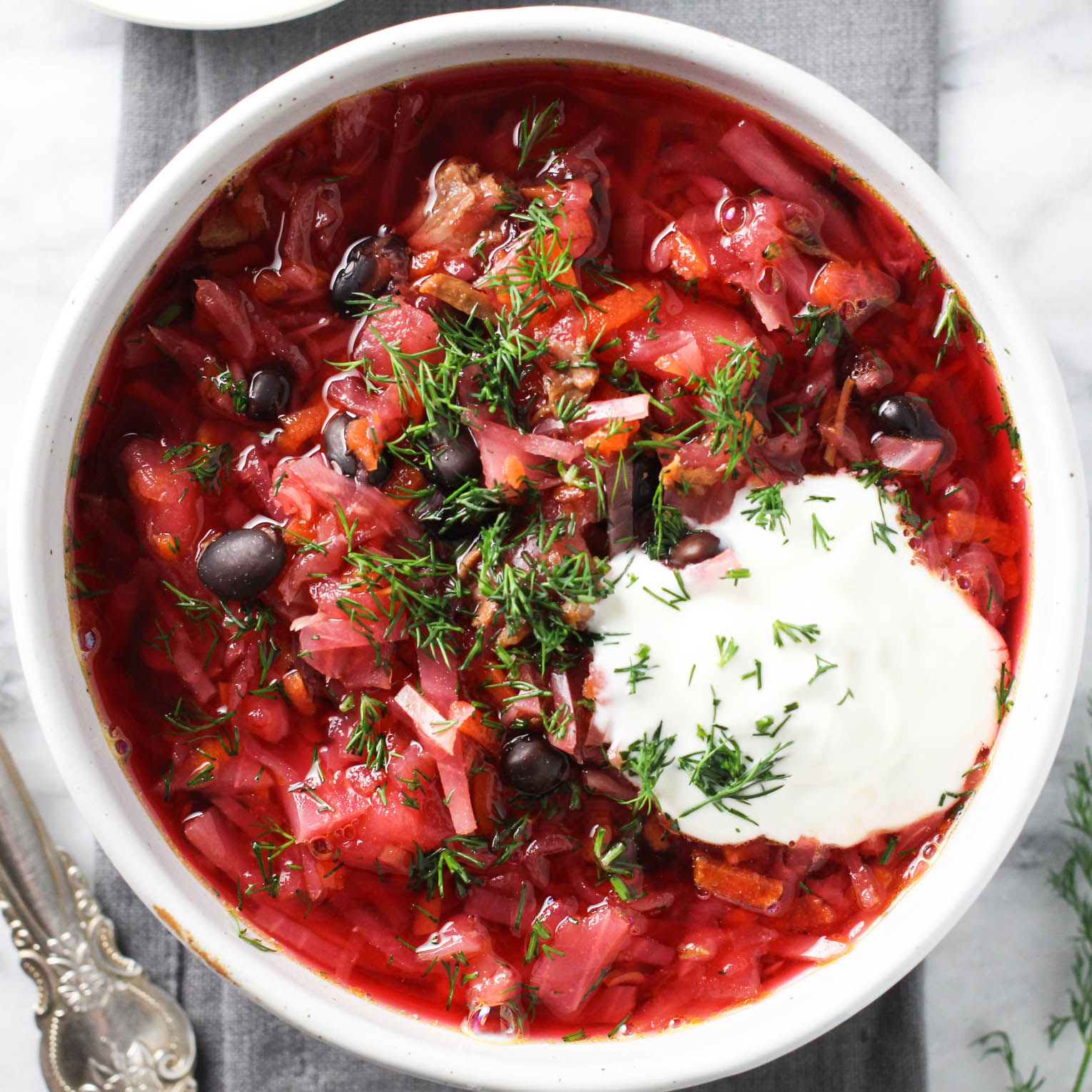Overhead shot of borscht in a bowl garnished with sour cream and chopped dill.