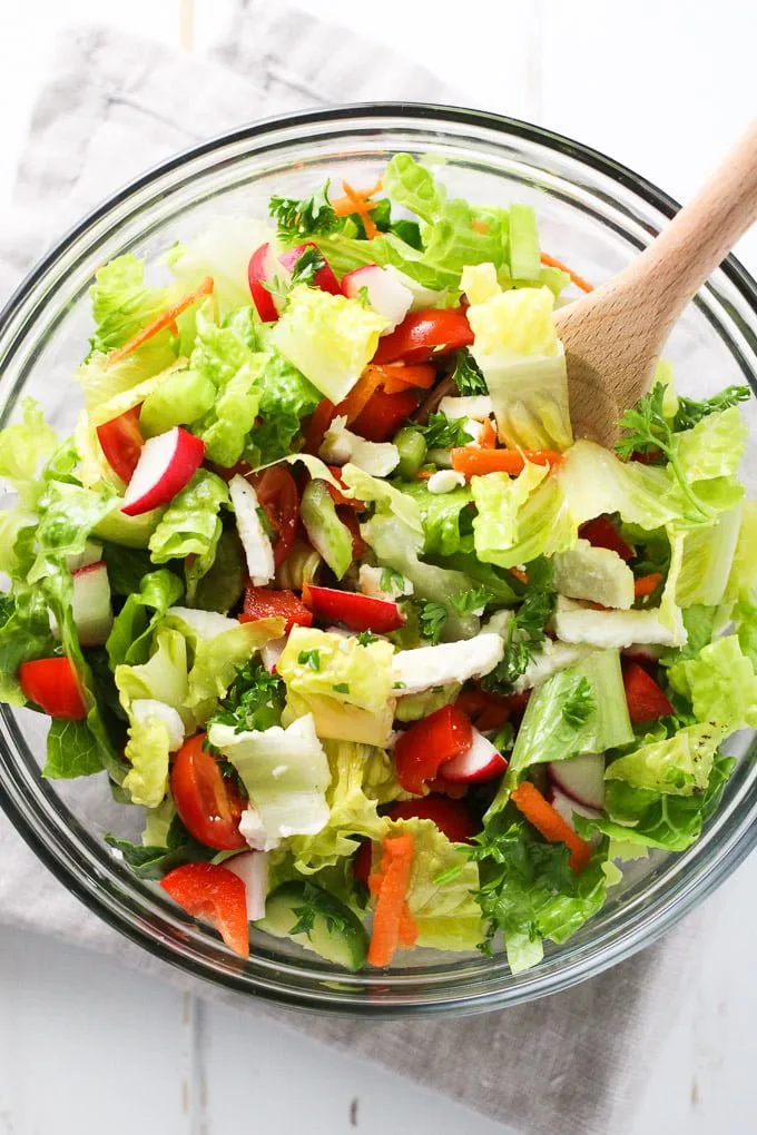 Romaine salad with chopped veggies and feta in a glass bowl. Top view.