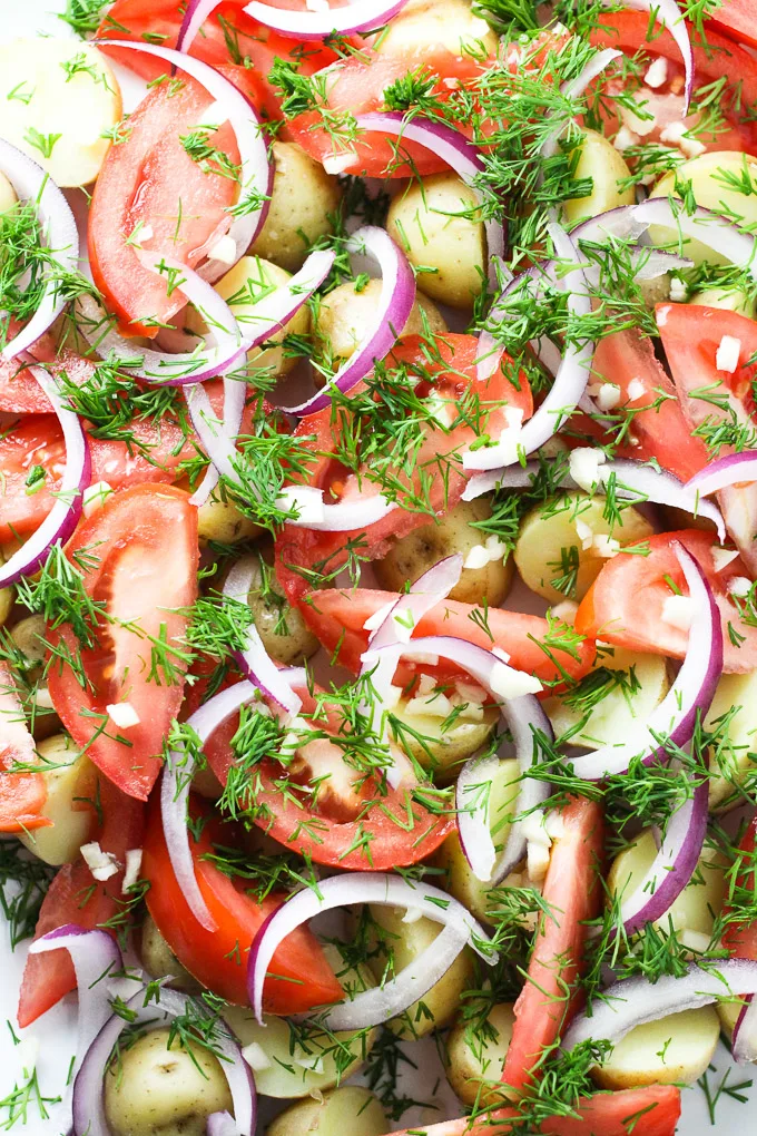 Close up of the potato salad with red onions, dill, tomatoes, and minsed garlic. 