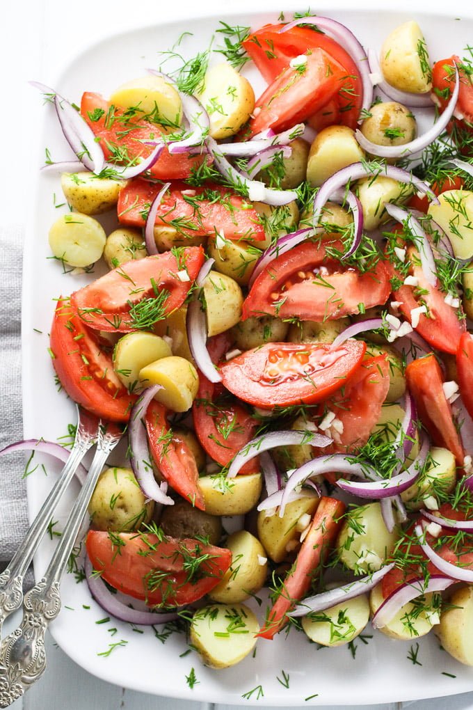 New potato salad with tomatoes and dill on a white platter.