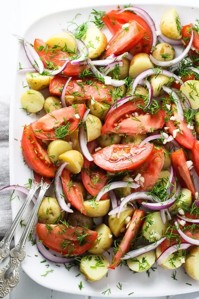 New potato salad with tomatoes and dill on a white platter.