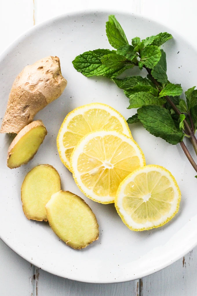 Ginger and lemon slices and mint leaves on a white plate.
