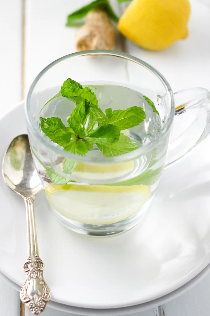 Homemade ginger tea with mint and lemon in a mug with a silver spoon on the left.