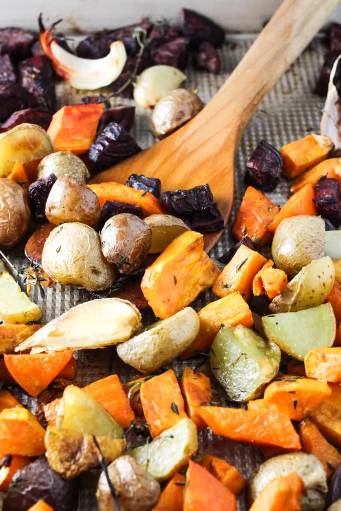 Roasted vegetables on a baking sheet being scooped with a wooden spatula.