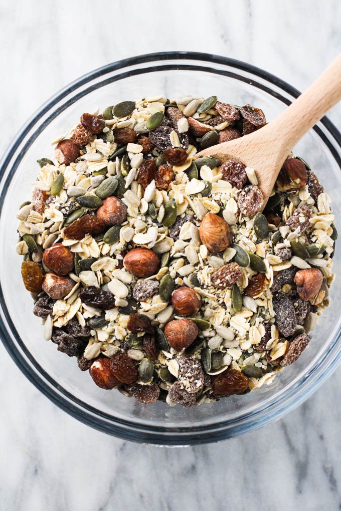 The homemade muesli mix in a glass bowl with a wooden spoon.