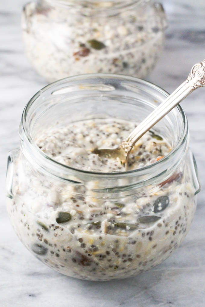 Soaked muesli in a glass jar with a silver spoon in it.