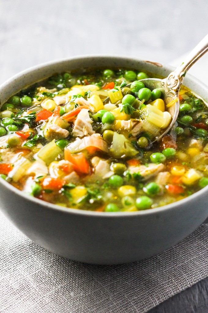 Chicken vegetable soup in a bowl with a sliver spoon scooping the soup.