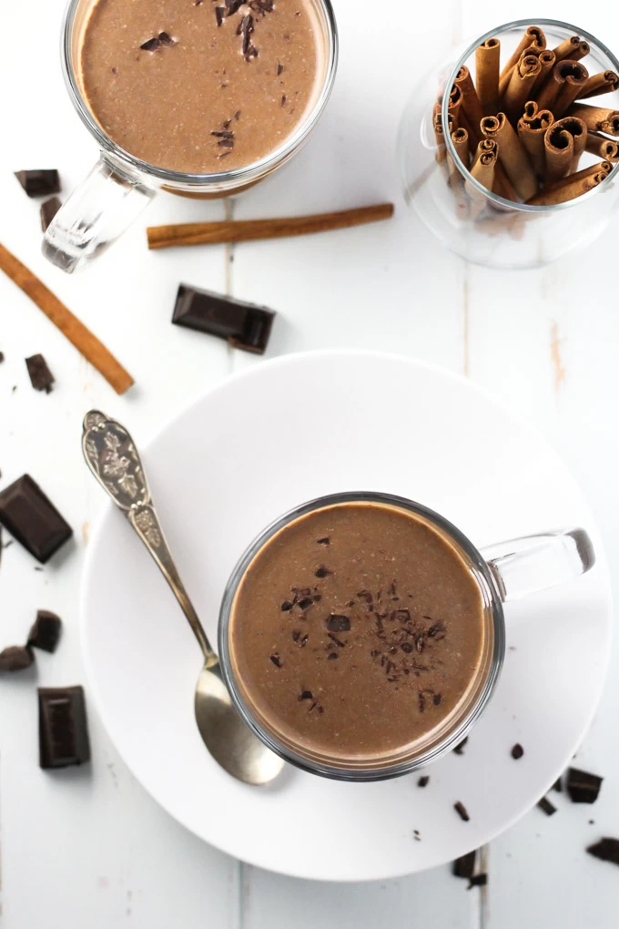 Hot chocolate in mugs, chocolate pieces, and cinnamon sticks on white background.