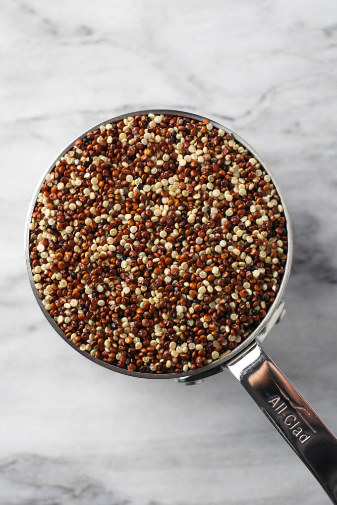 Overhead shot of quinoa in a measuring cup standing on a marble background.