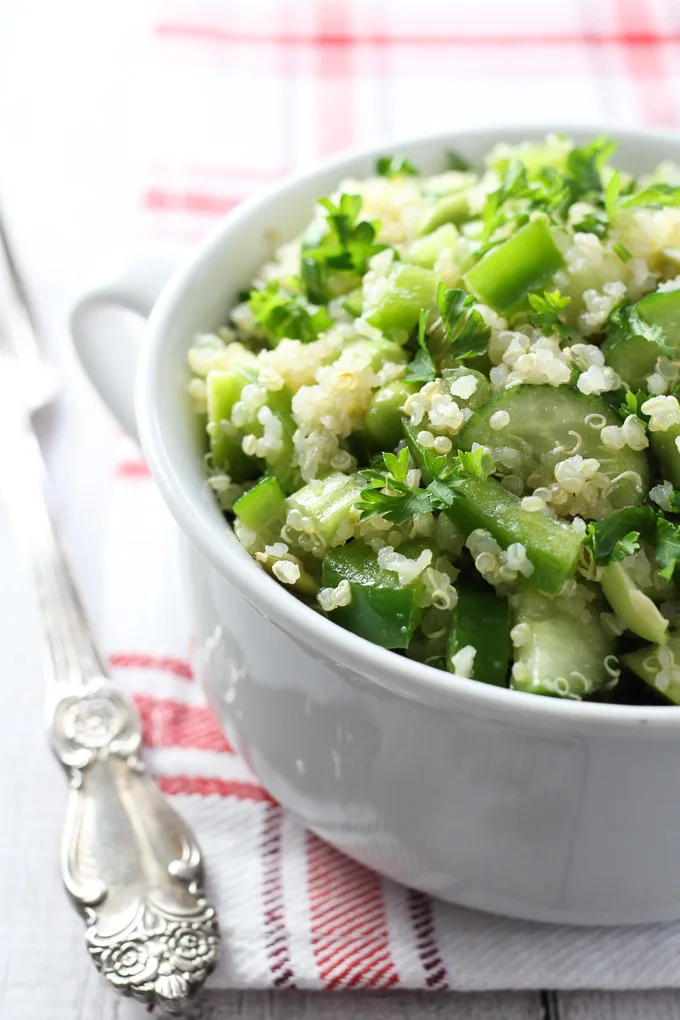 Quinoa salad with green vegetables in a white bowl. A silver fork to the left.