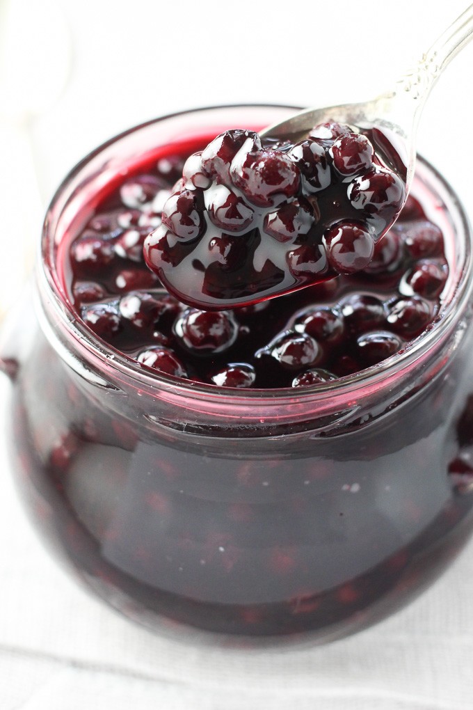 Blueberry sauce in a spoon. Glass jar in the background.