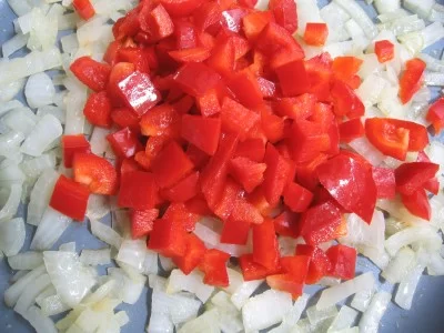 Onion and bell peppers in a frying pan.