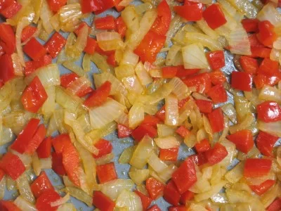 Sauteed onions and red bell peppers in a frying pan.