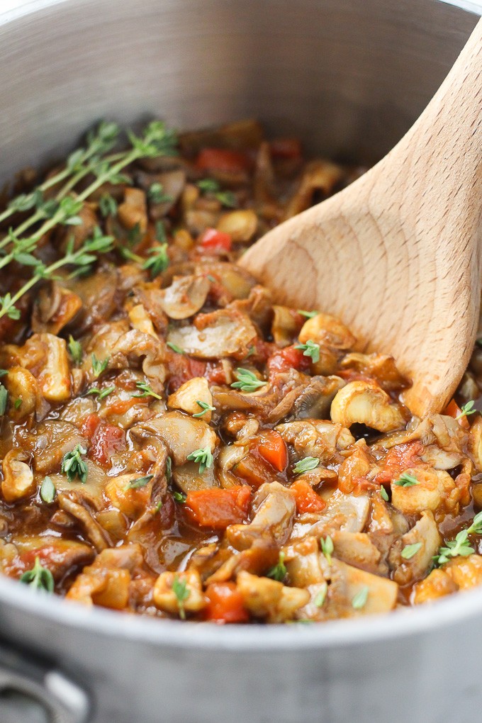 Vegan mushroom goulash in a pot with a wooden spoon. Side view.