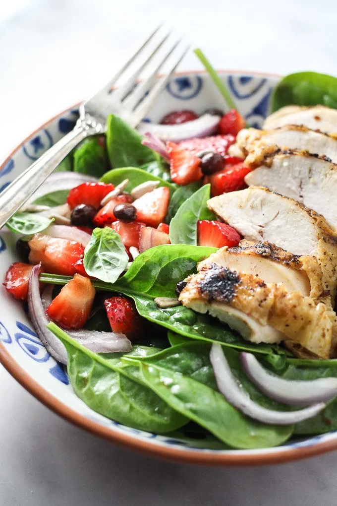 Spinach salad with chicken and strawberries in a bowl.