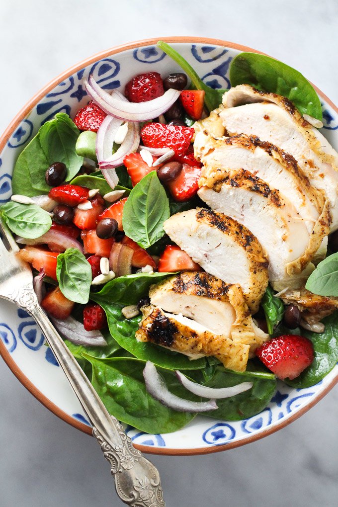 Spinach salad with chicken and strawberries in a bowl with a silver fork. Top view.