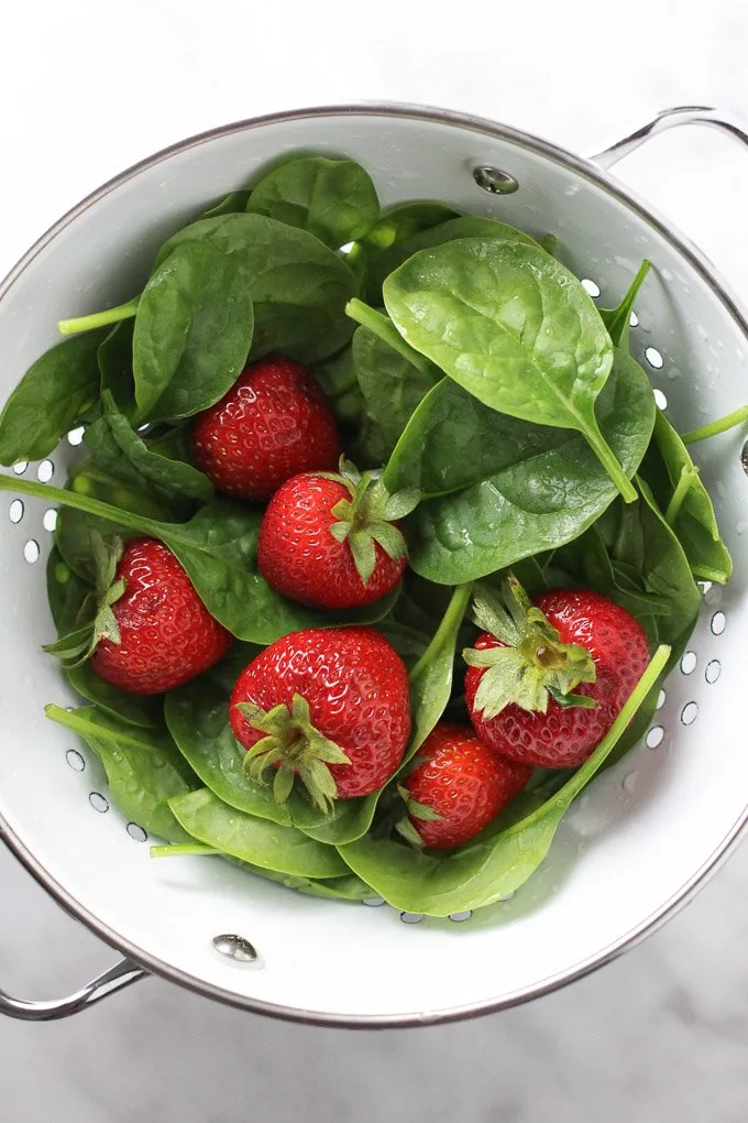 Spinach and strawberries in a white colander.