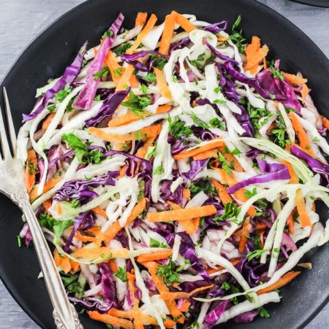 Overhead shot of the red and green cabbage salad on a black plate. Silver spoon to the left.