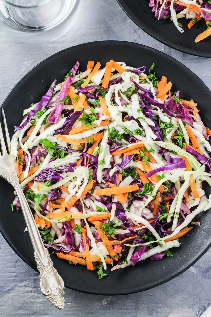 Overhead shot of the red and green cabbage salad on a black plate. Silver spoon to the left.