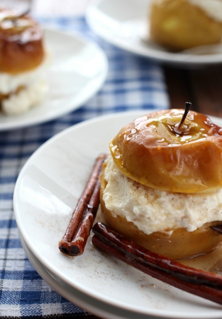 Baked apples with ricotta cheese on white plates. Garnished with cinnamon sticks.