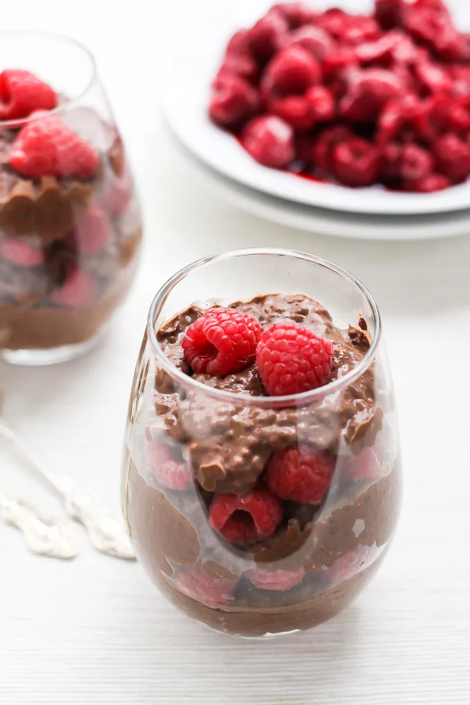 Chocolate chia pudding with raspberries in a dessert glass. Fresh raspberries on a plate in the background.
