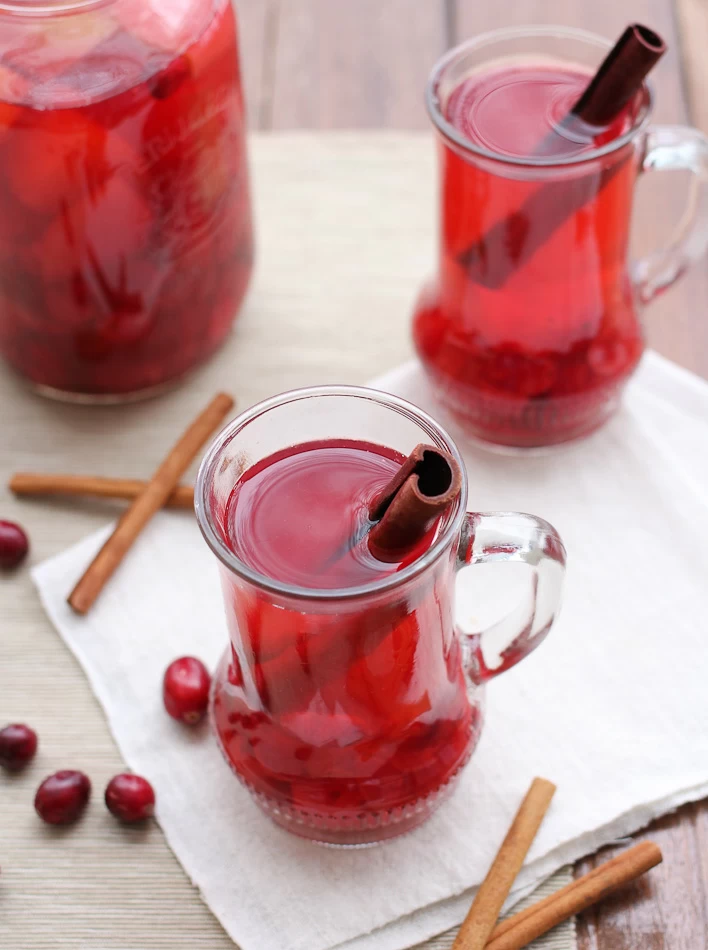 Cranberry punch in glass mugs garnished with cinnamon sticks.