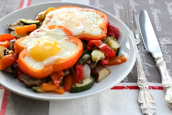 Sunny side eggs with vegetable served on a white plate with a fork and knife to the right.