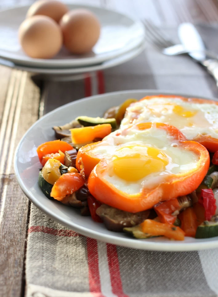 Sunny side up eggs with vegetables served on a white plate.