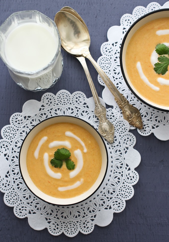 Overhead shot of red lentil soup in bowls, a glass of milk and two spoons.