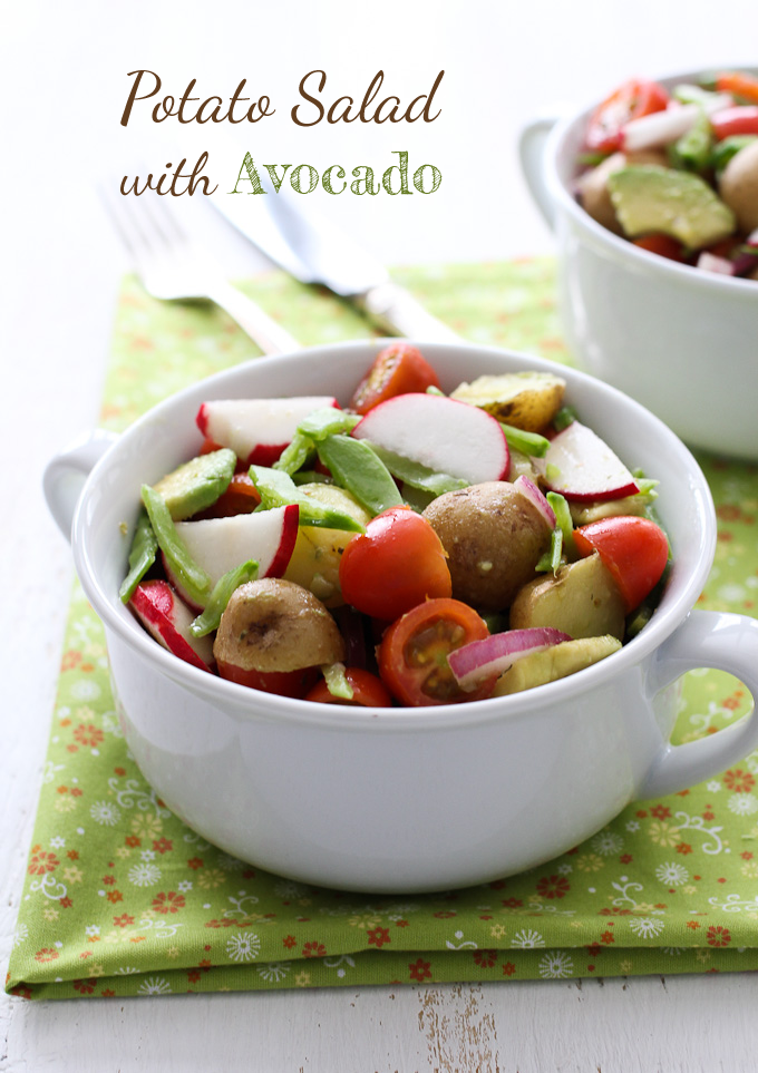 Potato salad with avocado in a white bowl standing on a green napkin.