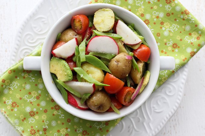 Overhead shot of the avocado potato salad in a bowl standing on a plate with a green napkin.