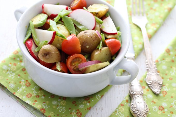 Potato salad with avocado in a bowl with silver fork and knife on the right side.