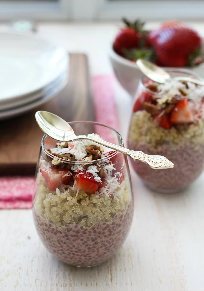 Strawberry chia and quinoa layered in a glass. Strawberries and plates in the background.