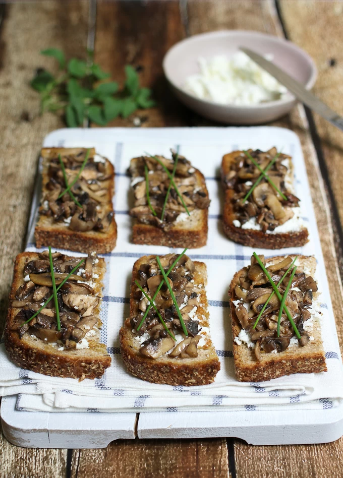 Goat cheese and mushroom crostini on a wooden board. Garnished with chives.