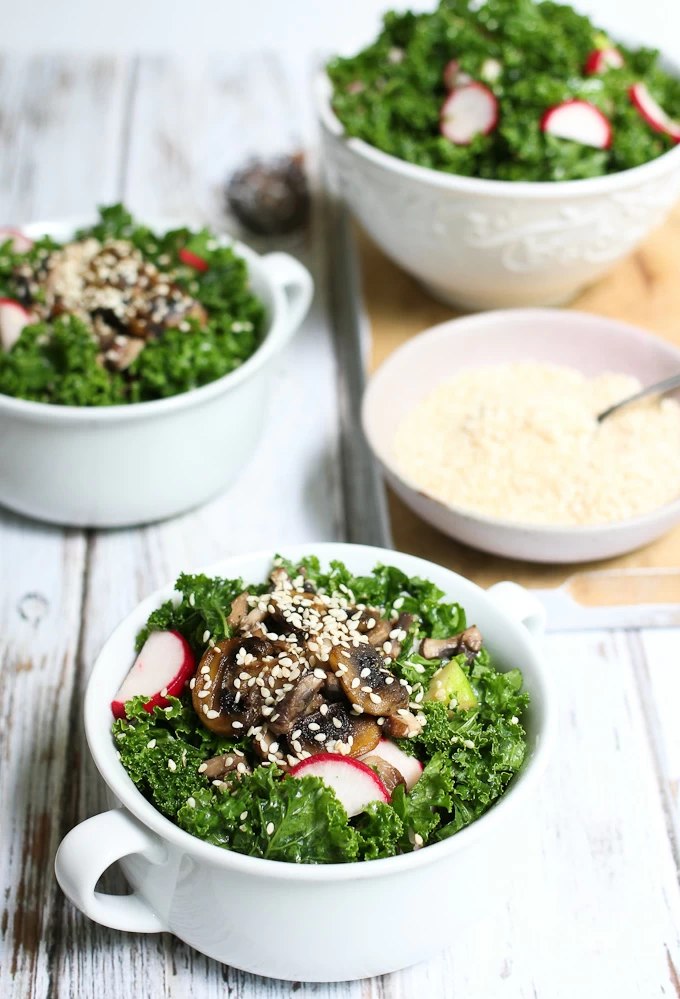 Kale salad topped with mushrooms and sesame seeds in white bowls.