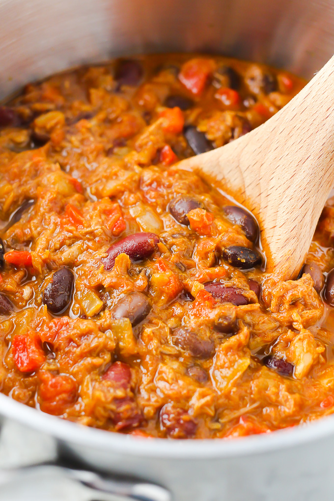 Close up shot of tuna chili in a pot with a wooden spoon in the chili.