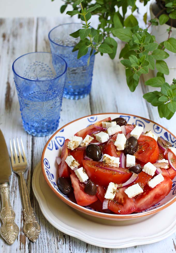 Tomato salad in a bowl. Two blue glasses of water and an origano plant in the background.