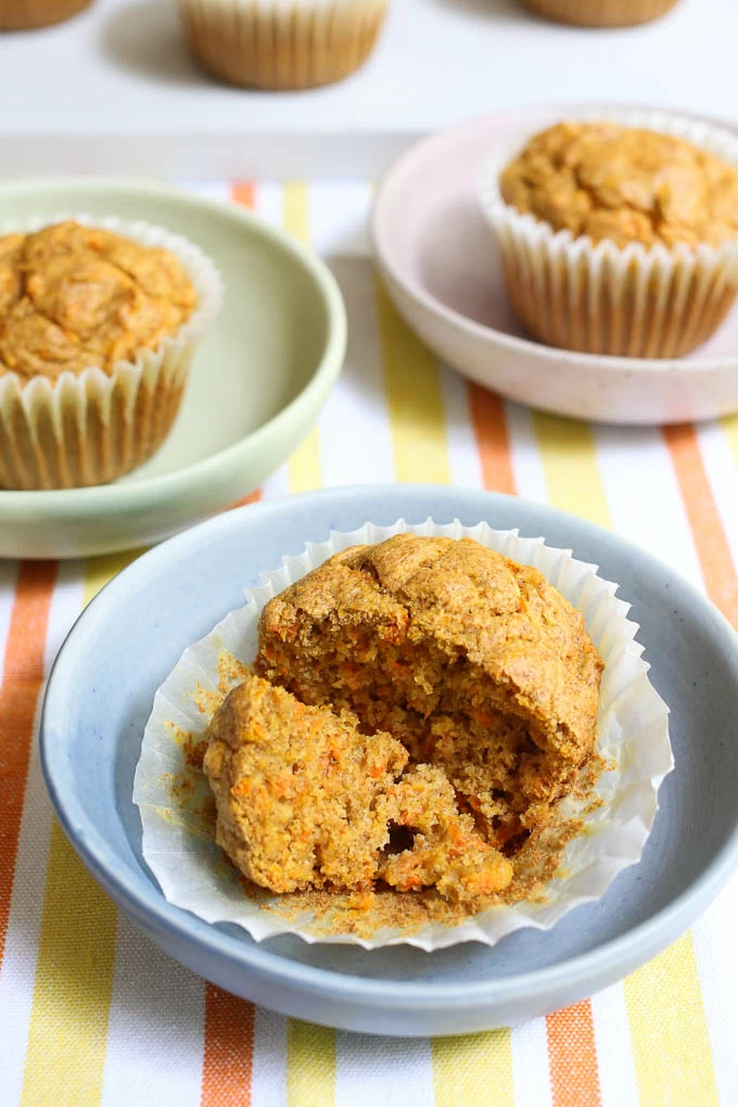 Close up of broken up carrot muffin on a plate. Two muffins on plates in the background.