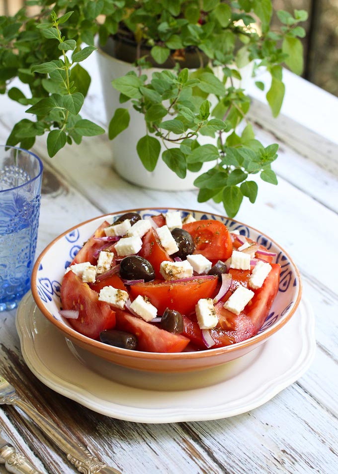 Mediterranean tomato salad in a bowl on a wooden table. Oregano plant in the background.