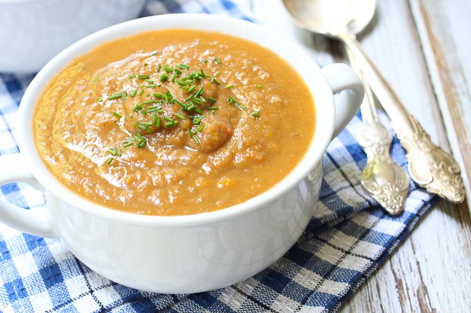 Close up shot of the eggplant vegetable soup in a white bowl. Two silver spoons to the right of the bowl.