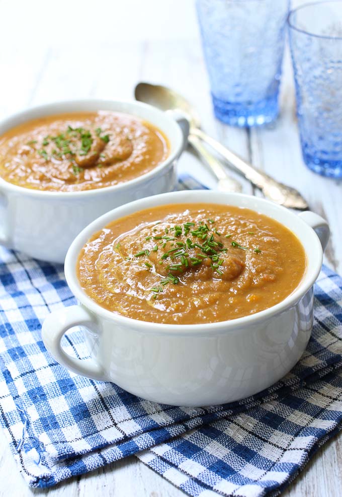 Two white bowls with the eggplant vegetable soup standing a tea towel.