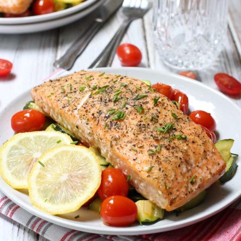 Roasted salmon with vegetables served on a white plate with lemon slices to the left.