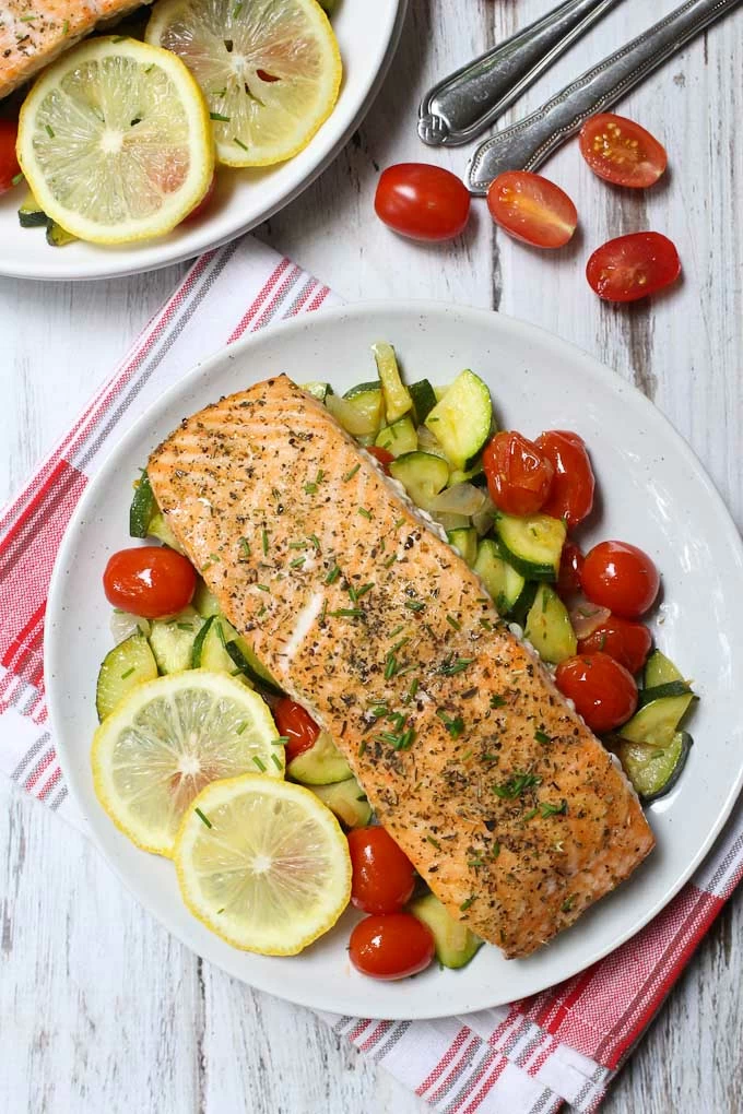 Roasted salmon with sauteed zucchini and tomatoes on a white plate.
