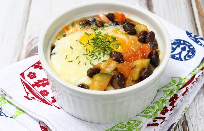 Baked eggs with beans and veggies in a ramekin standing on a tea towel.