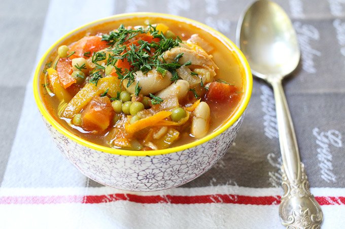 Chicken and white bean soup in a bowl. A silver spoon to the right.