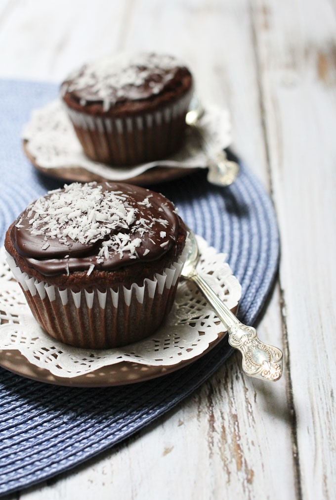 Vegan chocolate cupcakes on a blue place mat. Silver spoons to the right.