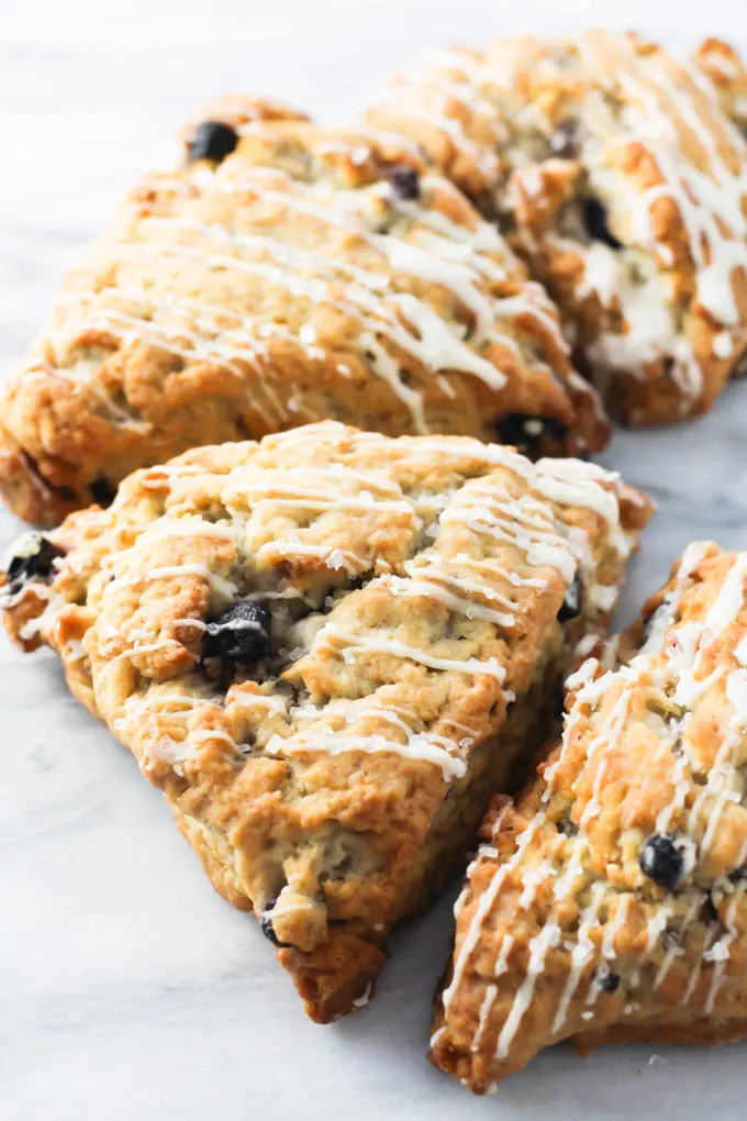 Blueberry scones on marble background. The scones are drizzled with glaze. 