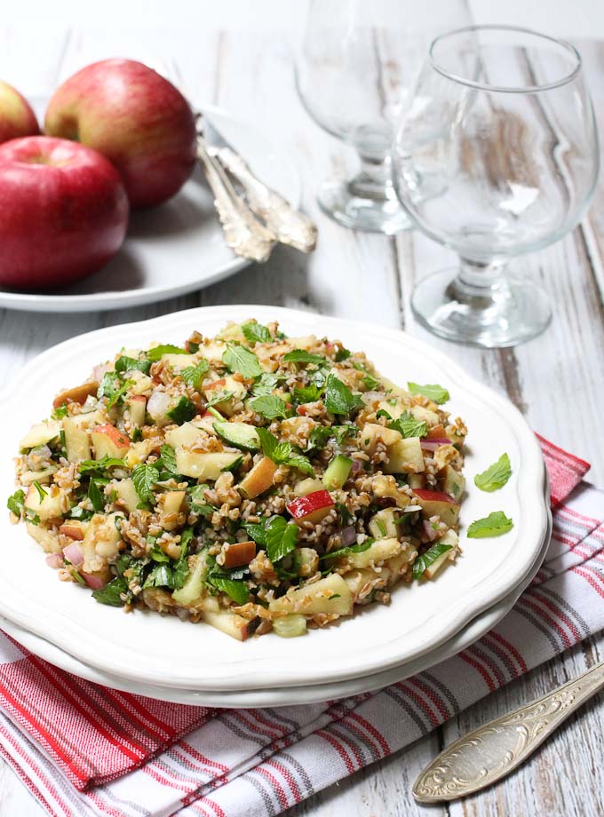 Bulgur salad on on a white plate. Apples in the background and wine glasses in the background..