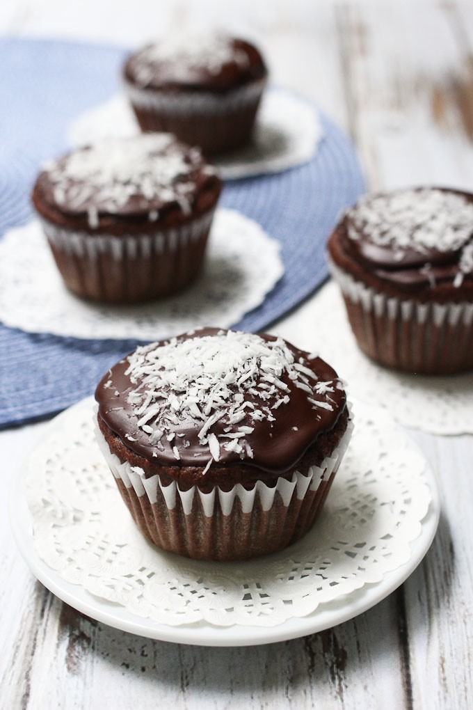 Vegan chocolate cupcake on a white saucer. More cupcakes in the background.