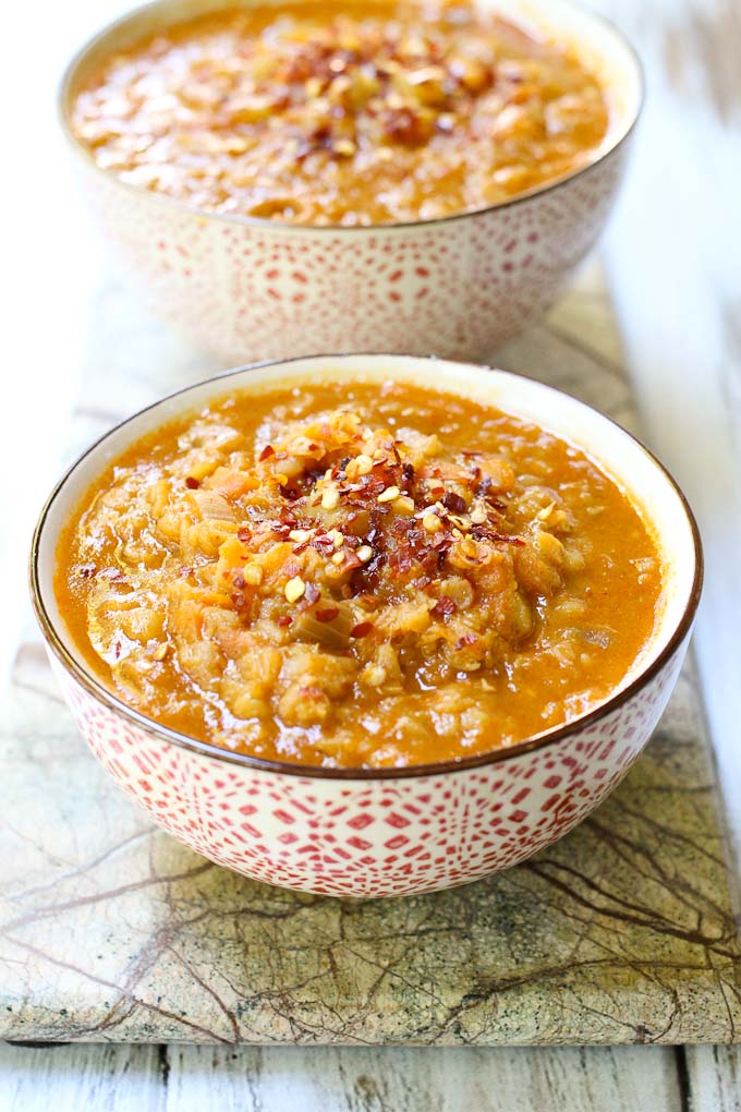 Two bowls with red lentil soup garnished with red pepper flakes.